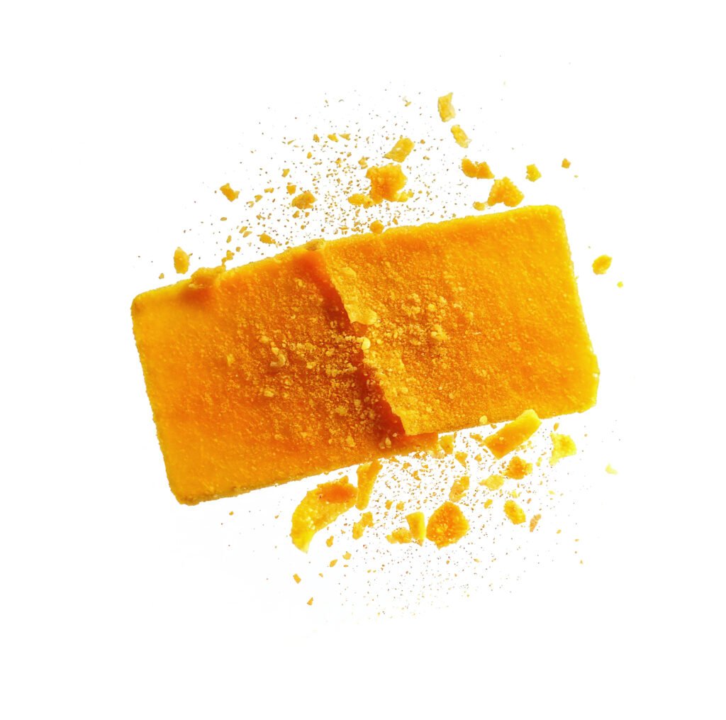 Bright yellow-orange freeze-dried mango bar with crumbly texture and powder coating, isolated on white background.